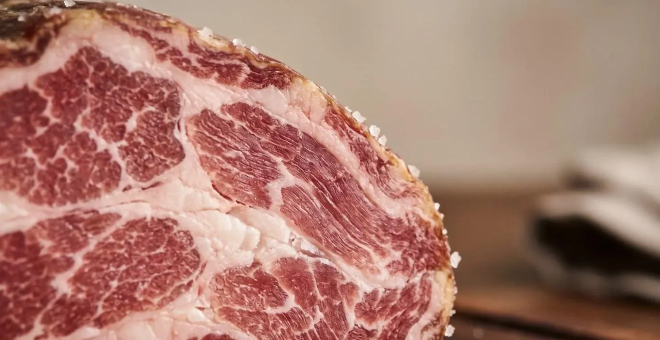 Détail macro d'une tranche de charcuterie corse artisanale montrant la texture marbrée et les cristaux de sel