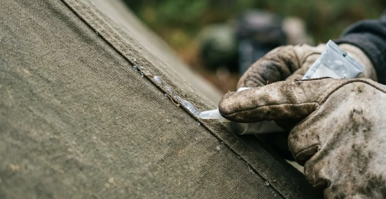 Gros plan sur une main appliquant un produit d'étanchéité sur la couture d'une toile de tente en conditions de bivouac
