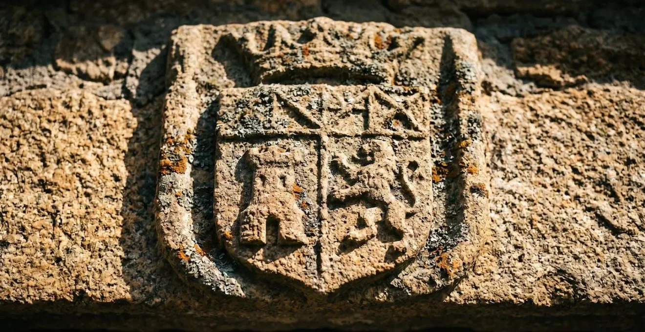 Gros plan sur un blason ancien gravé dans la pierre de granit, éclairé par une lumière rasante révélant les détails érodés du relief héraldique